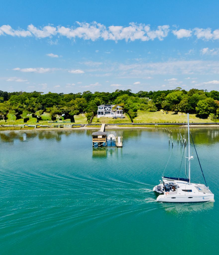 Aerial view of waterfront estate dock with sailboat passing by